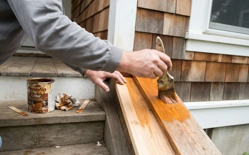 A homeowner applies a fresh coat of protective stain to cedar siding boards on an exterior wall of a Florida home